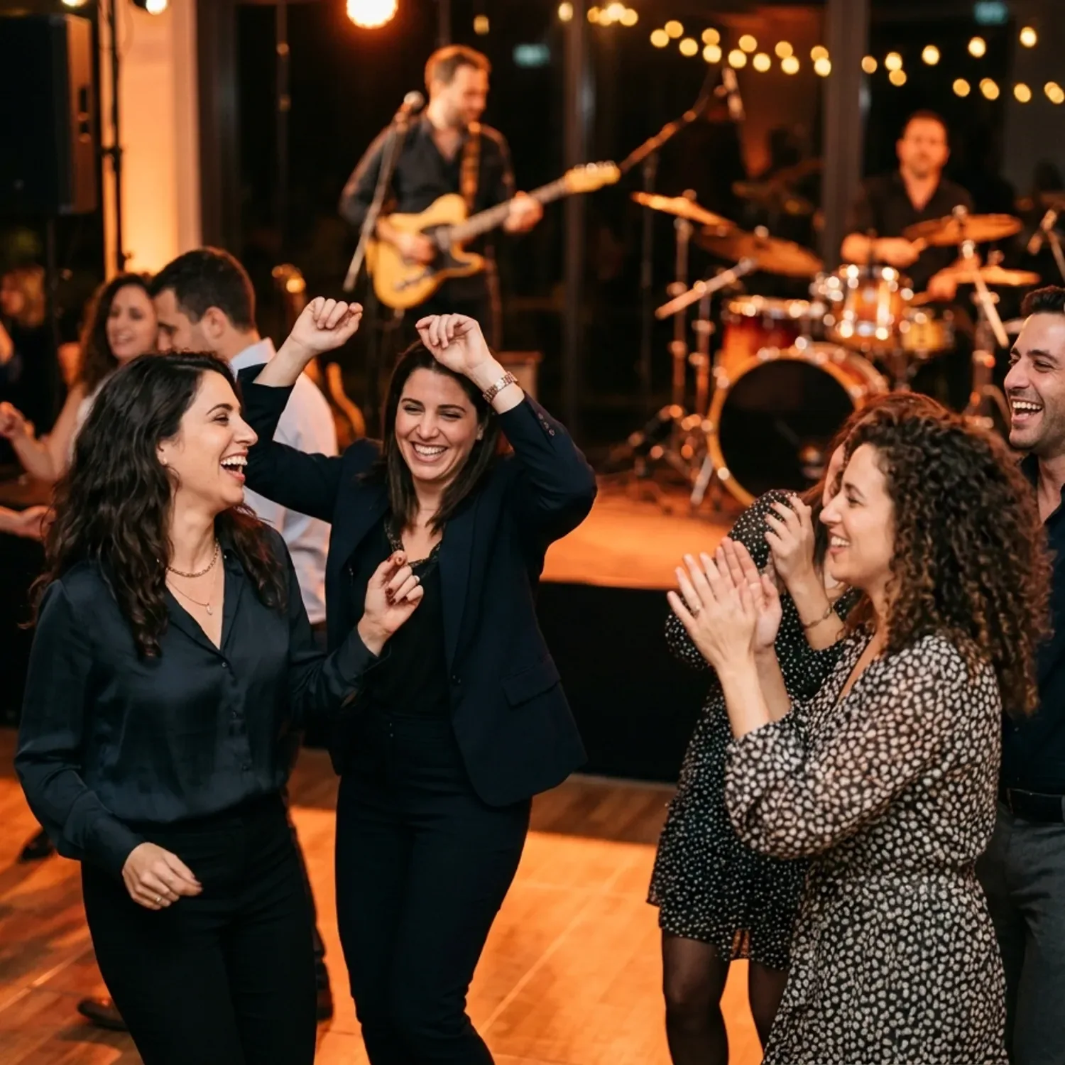 צילום ריאליסטי של עובדי חברה מחייכים ורוקדים ברחבת ריקודים, ברקע רואים במטושטש חברי להקה מנגנים על גיטרה ותופים תחת תאורה חמה של אירוע ערב.