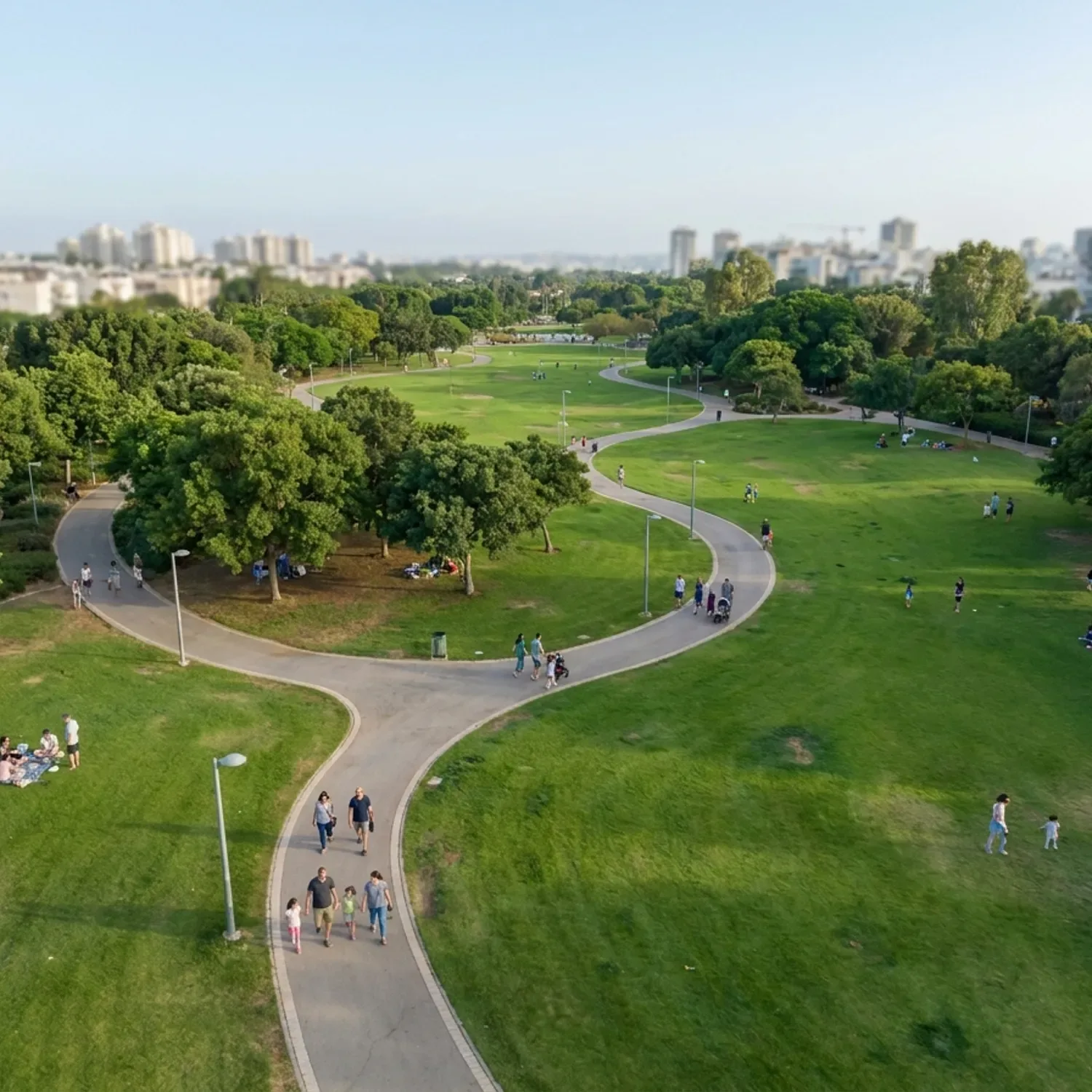 צילום רחפן מציאותי באור יום טבעי של פארק עירוני ירוק ורחב ידיים בישראל, עם מדשאות מטופחות, שבילי הליכה מתפתלים, עצים מצלים ומשפחות ישראליות בלבוש יומיומי מטיילות בשבילים, זווית גבוהה ופתוחה